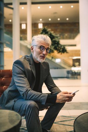Portrait of mature businessman sitting in office lounge with mobile phone