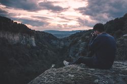 man with photo camera sitting on hill mountain with magnificent sunset