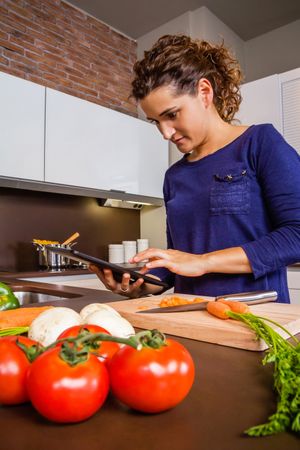 Woman checking digital tablet for instructions as she prepares dinner
