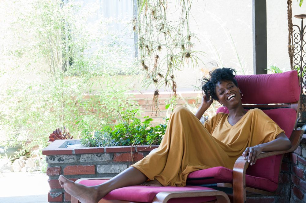 Full length shot of woman in yellow dress outside under covered patio laughing with eyes closed
