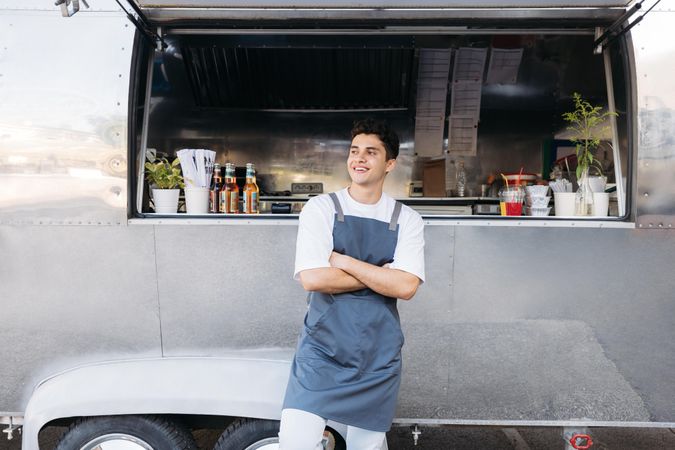 Smiling man in apron outside of food truck with arms crossed