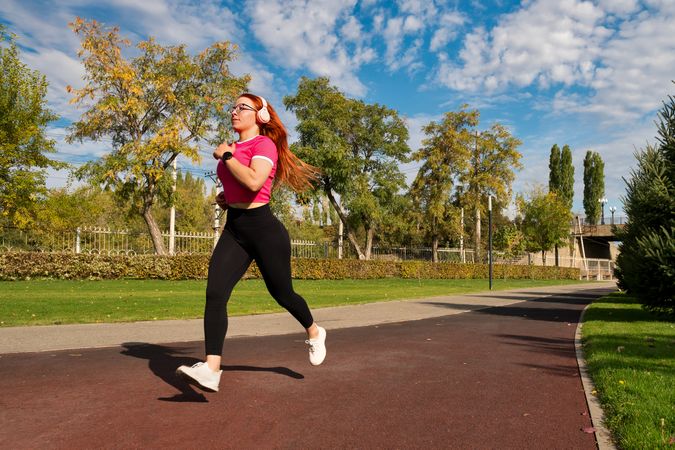 Woman running in park, listening to music, wearing sportswear