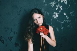 Studio portrait of woman with blue eyes holding gerbera flower against dark floral wall