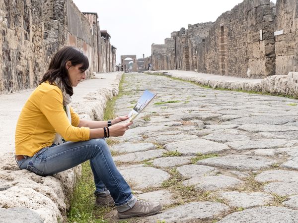 Side view of a woman in yellow checking tourist map of ancient ruins