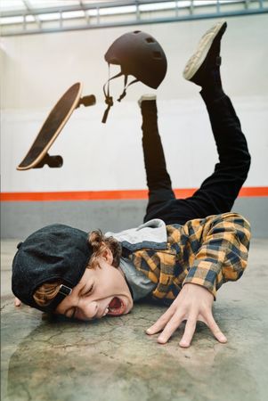 Boy falling from skateboard on concrete ground
