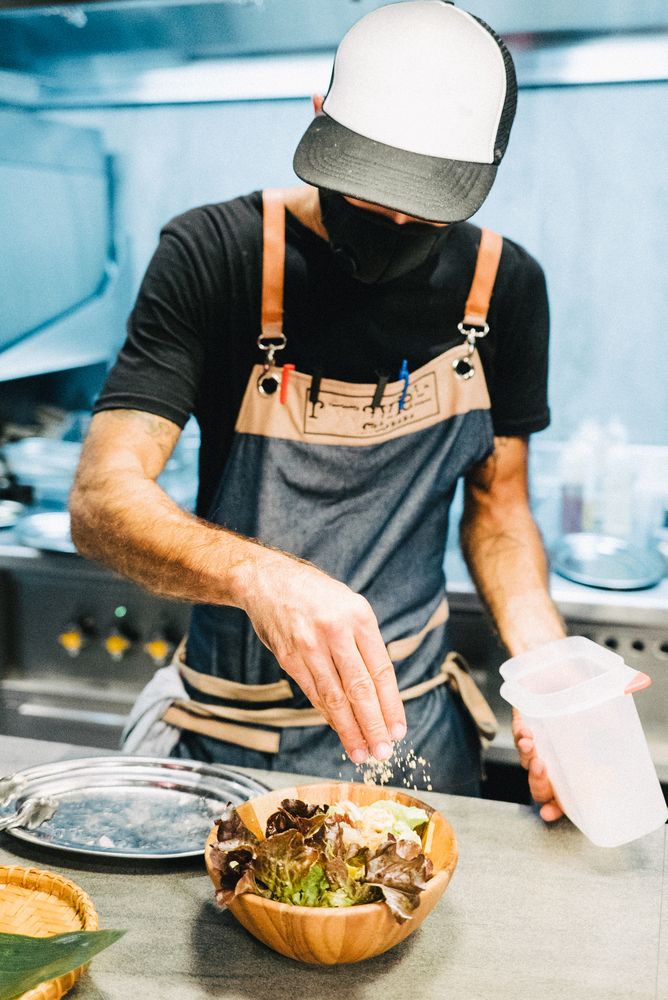 Chef with mask putting crumbs on salad