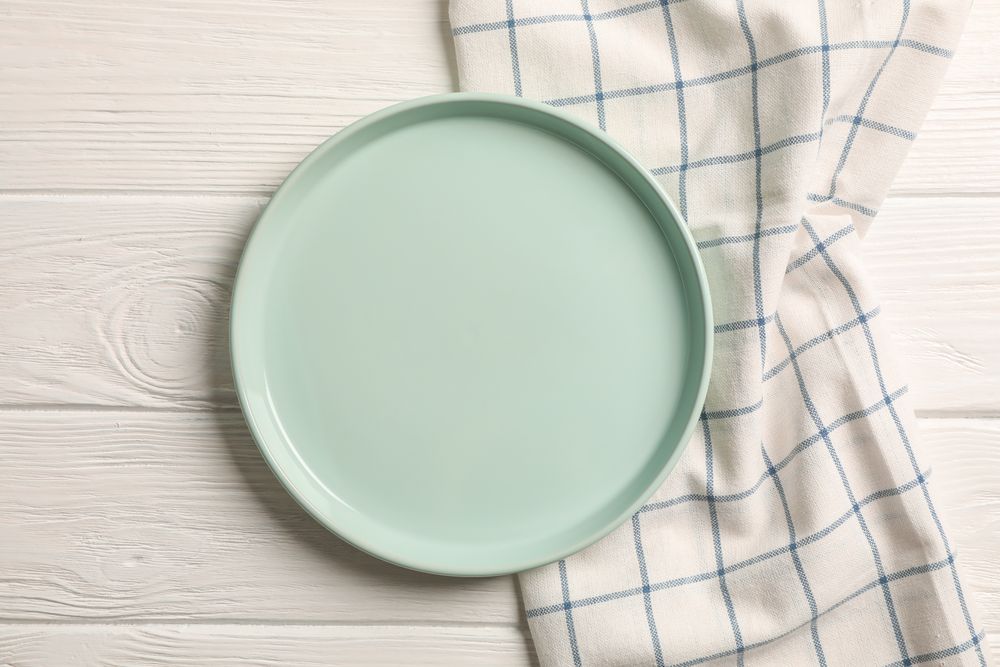 Kitchen towel with plate on wooden background, top view