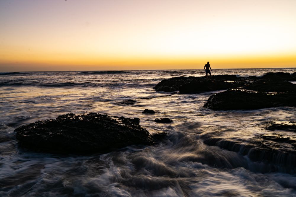 Silhouette of person standing on rock on sea during sunset