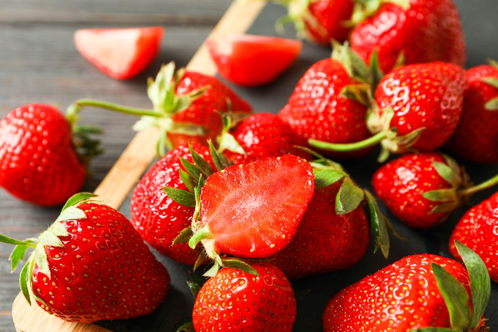 Cutting board and fresh strawberries on wooden table, closeup and space for text. Summer sweet fruits and berries