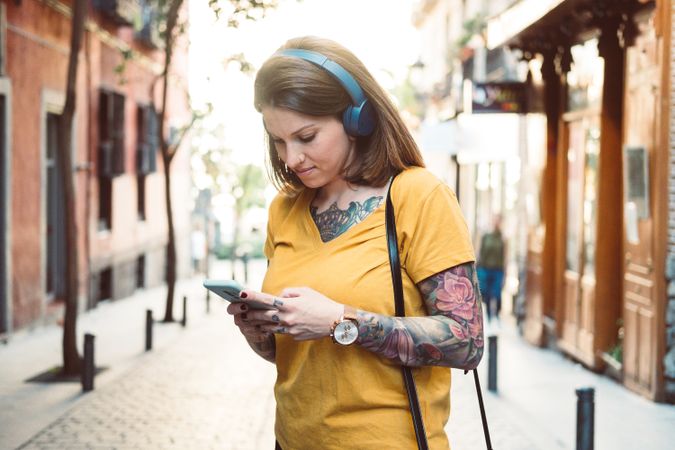 Inspired woman in headphones listening to music on smartphone on street