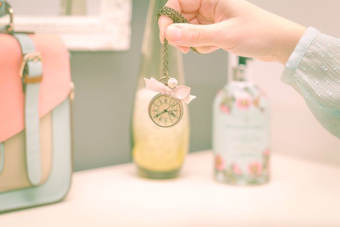 hand holding a vintage clock necklace in front of female complements in soft pastel colors