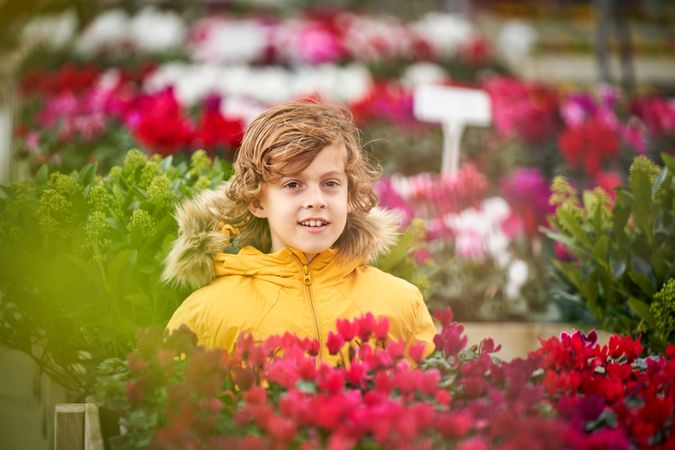 Positive preteen boy near blooming bright flowers in pots