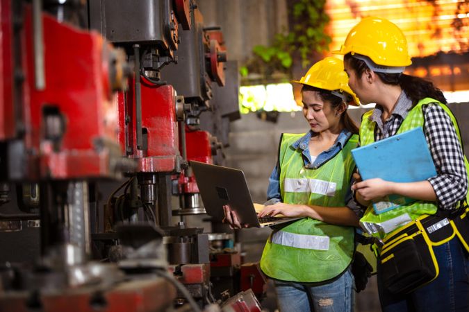 Two female engineers or technician worker wearing safety hard helmet discuss project at work