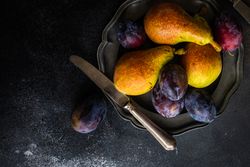 Top view of pears and plums on dark plate