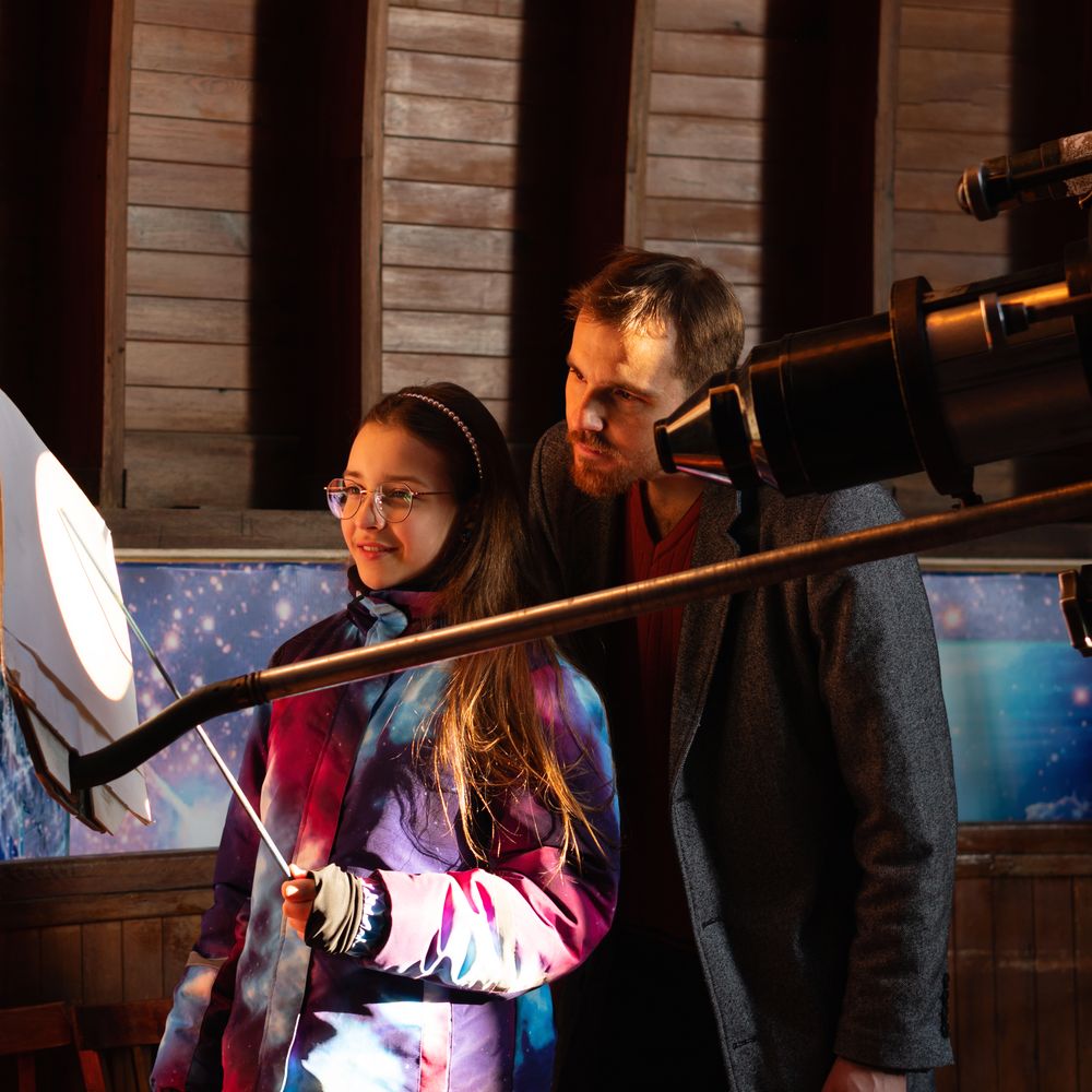 Mentor and student observe projected solar image through telescope.