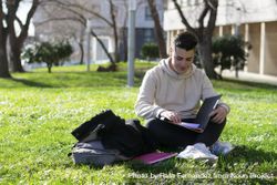 Young man sitting on the school grass while reading a book 0Ld19r
