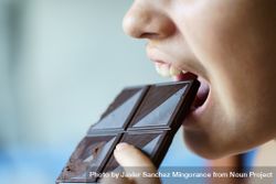 Side view of girl biting into square of dark chocolate 0gXO17