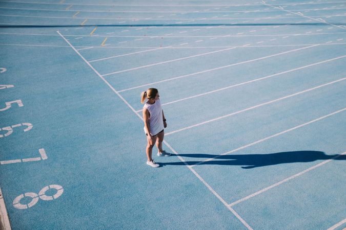 Young woman looking out at the lanes from the beginning of a track field