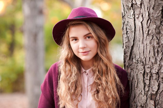 Portrait of teenage girl with purple hat standing beside tree