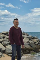 Middle aged man standing on rocky seashore
