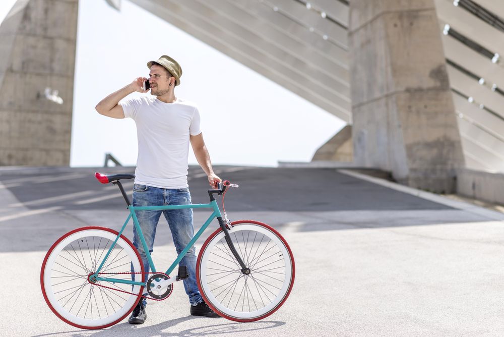 Male with bicycle speaking on phone under modern building