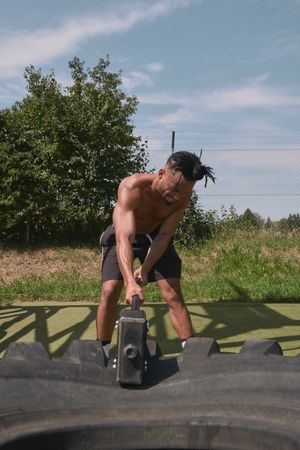 Muscular Black guy hammering tire in outdoor gym