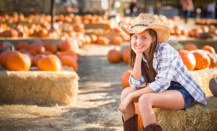 Girl Wearing Cowboy Hat Enjoying The Pumpkin Patch on a Sunny Fall Day.