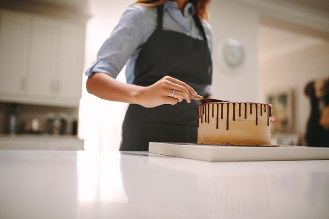 Cropped shot of female in apron preparing chocolate cake in kitchen