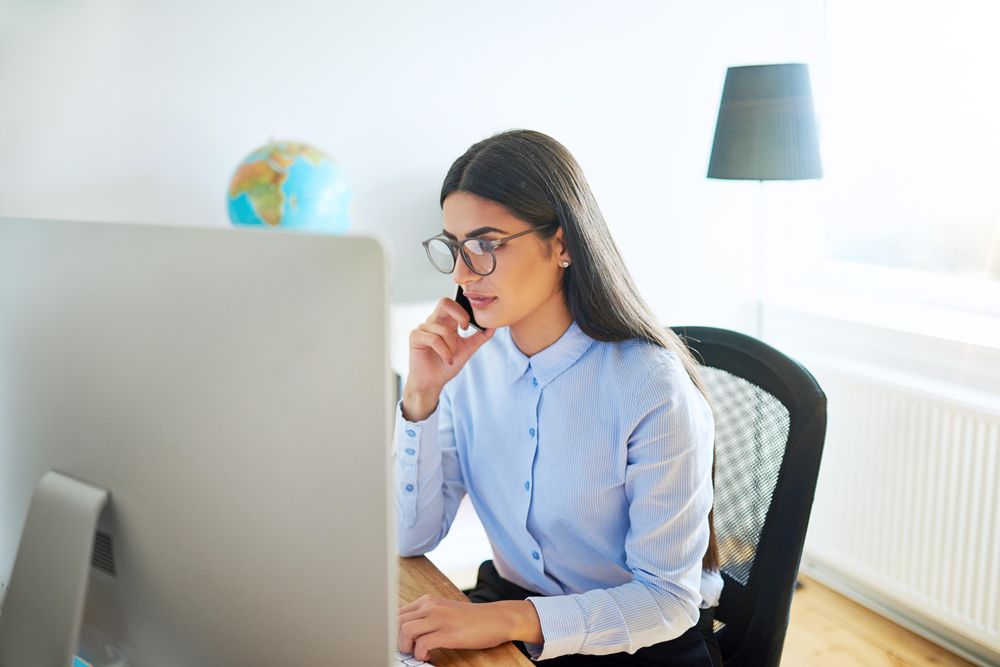 Female taking serious phone call in front of her computer in a bright office