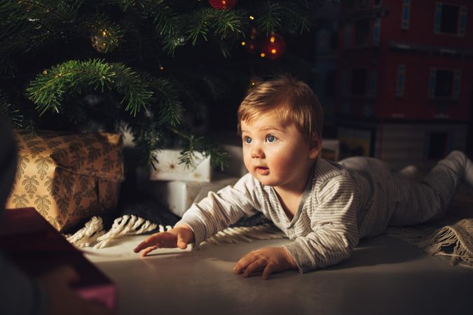 Cute baby boy lying by christmas tree at home