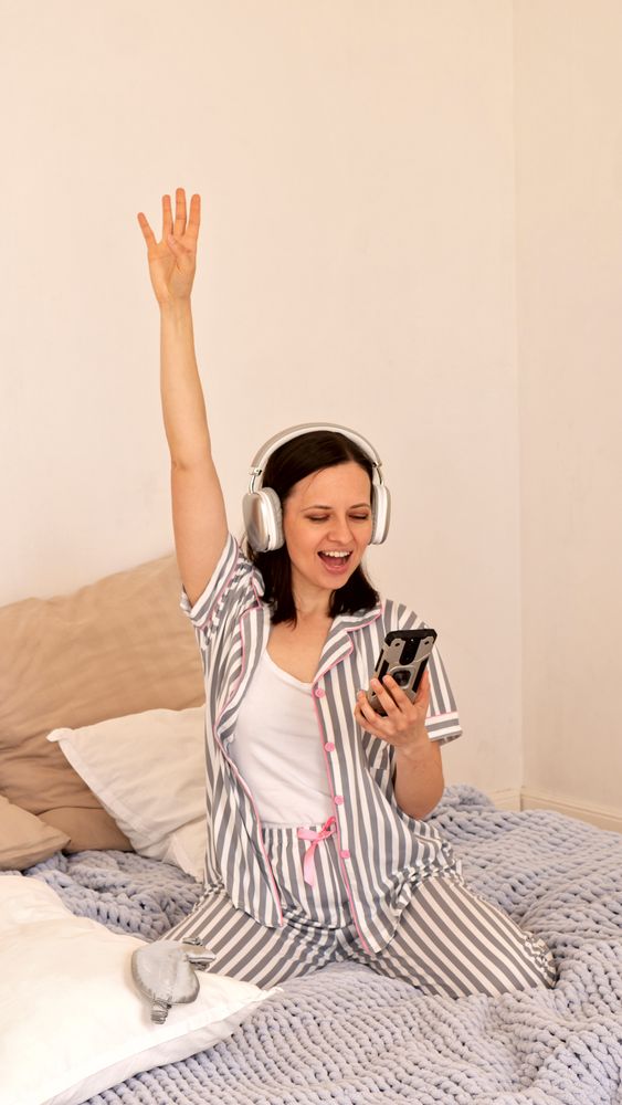 Woman with headphones celebrating, arm raised in bed.