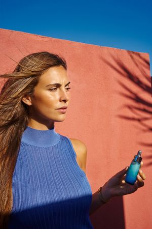 Woman on a red building holding perfume