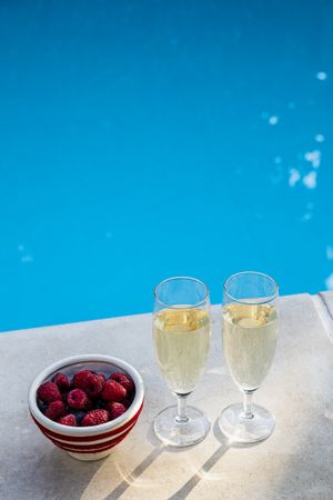 Two glasses of champagne and fresh berries by the pool, celebrating a summer holiday