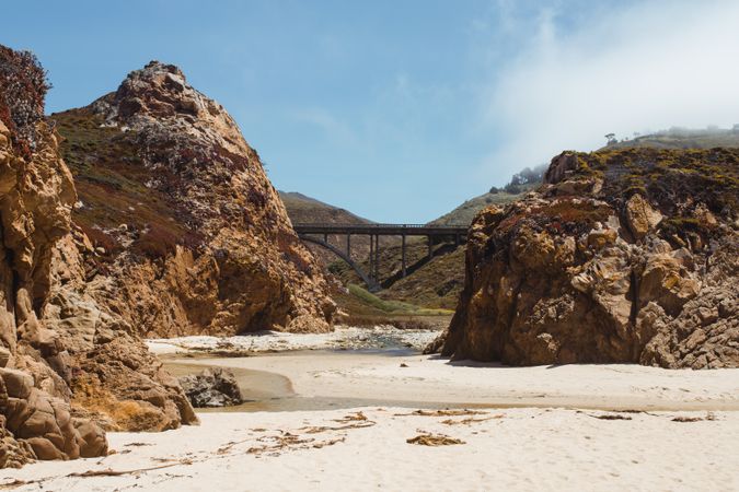 Empty stony rocky shore and bridge under light cloudy sky in Big Sur