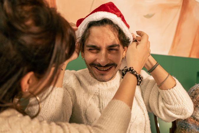 Playful woman putting a Santa hat on her laughing boyfriend at a Christmas party