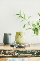 Iced matcha drink with creamer on side, with eco friendly straw and leaves
