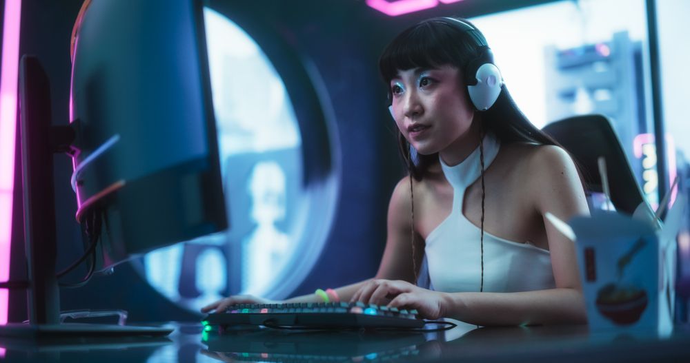 Stylish Asian Streamer Chats with Teammates Online while Playing Video Games on a Computer in a Futuristic Cyberpunk Technology Room