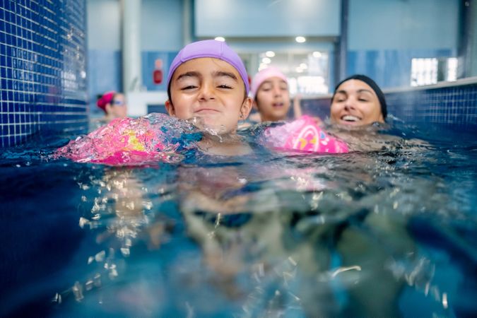 Cheerful girl in hat smiling and swimming in pool in water park
