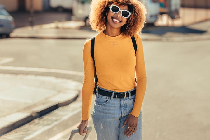 Smiling woman wearing sunglasses and a backpack walking on street