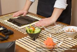 Hands of chef ready to prepare Japanese sushi rolls, with principal ingredients in the foreground 42aQm5