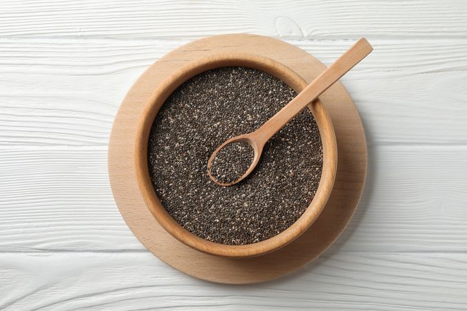 Wooden bowl with chia and spoon on wooden background, top view