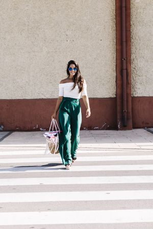 Stylish smiling woman with sunglasses holding a handbag while crossing the street