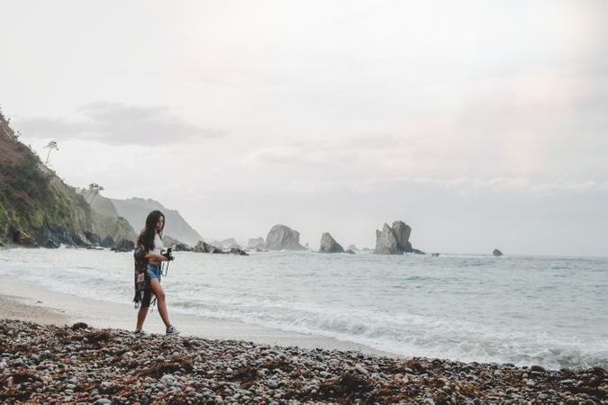 Woman with camera on shore near stones and water