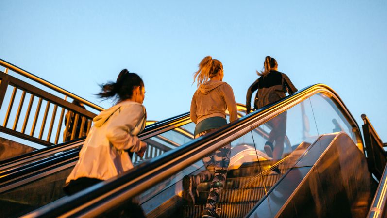 Women friends training running up escalator in city at sunset