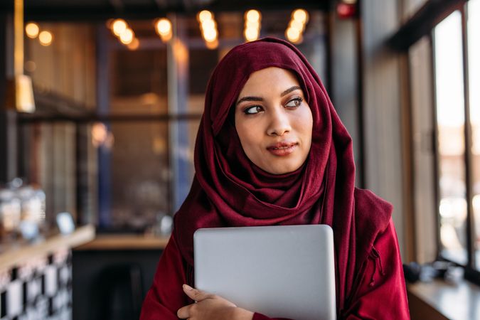 Businesswoman in hijab with laptop at cafe looking away