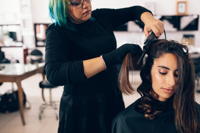 Salon hairdresser using curling wand to style customer’s hair