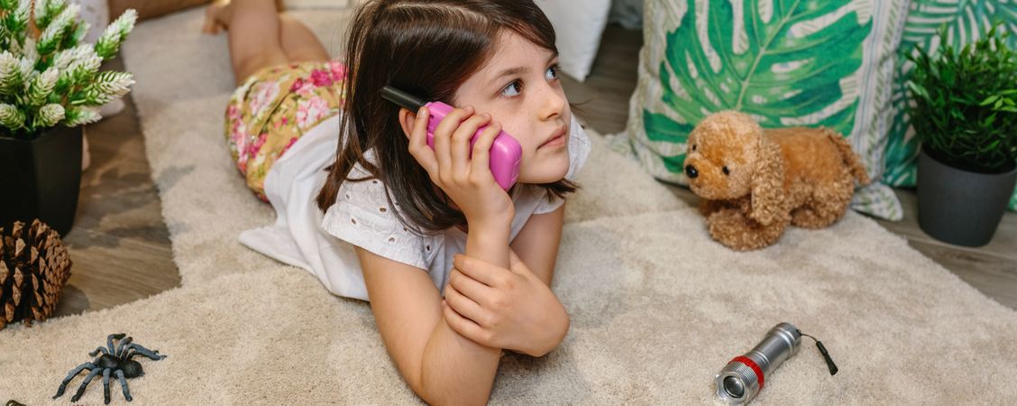 Banner of girl using walkie-talkie lying over rug surrounded by cushions and plants in teepee