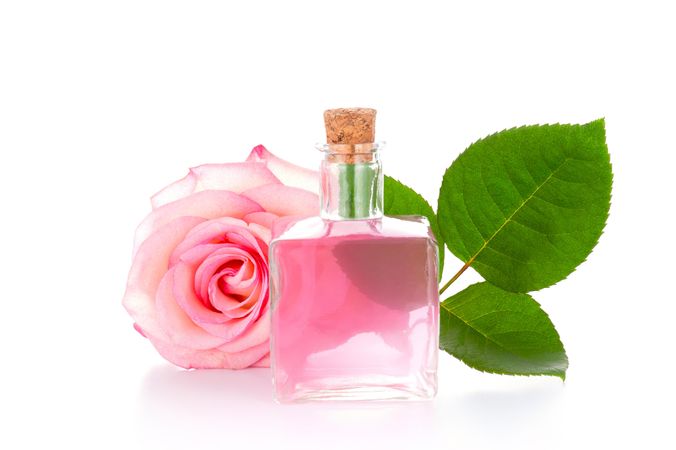 Rose water bottle on light background with rose and leaves