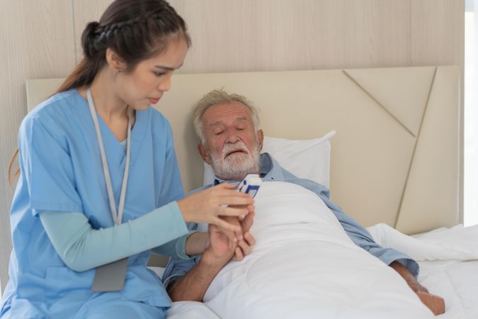 Asian nurse caregiver checking mature man’s oxygen with pulse oximeter