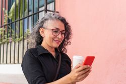 Hispanic woman sending message on cellphone while walking in the urban environment.